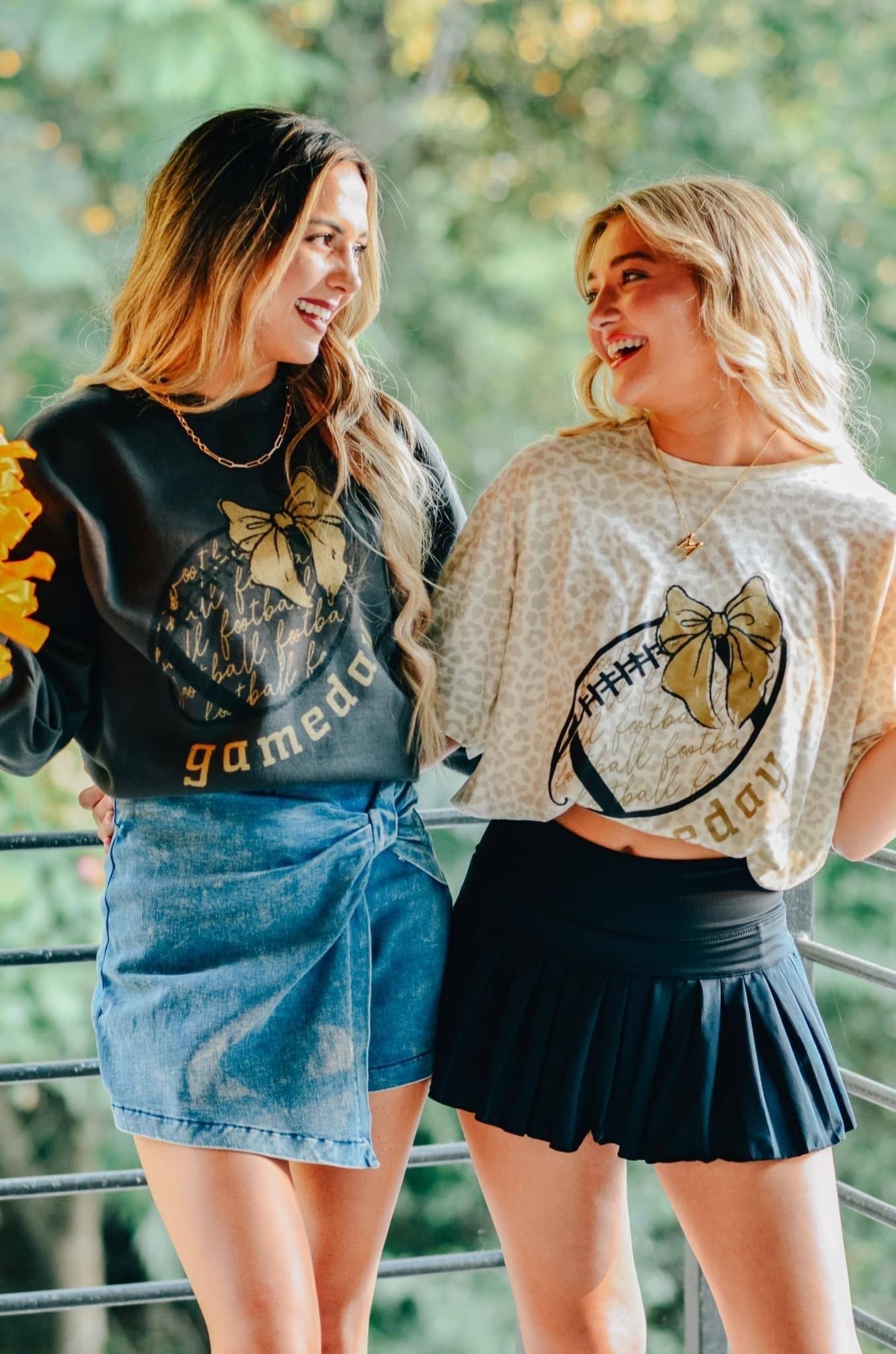 two models wearing gameday football clothes grey women's fleece sweatshirt with  gold bow and football written across in fancy script on the football