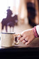 a medel hand with a cream colored coffee mug with black spots and red pink yellow and burgundy jelly loop hair ties spiral